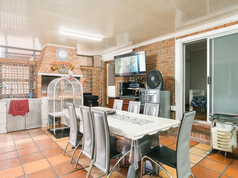Covered patio area featuring a built-in braai, brick wall finishes, and tiled flooring, providing a functional space for outdoor dining and entertainment.