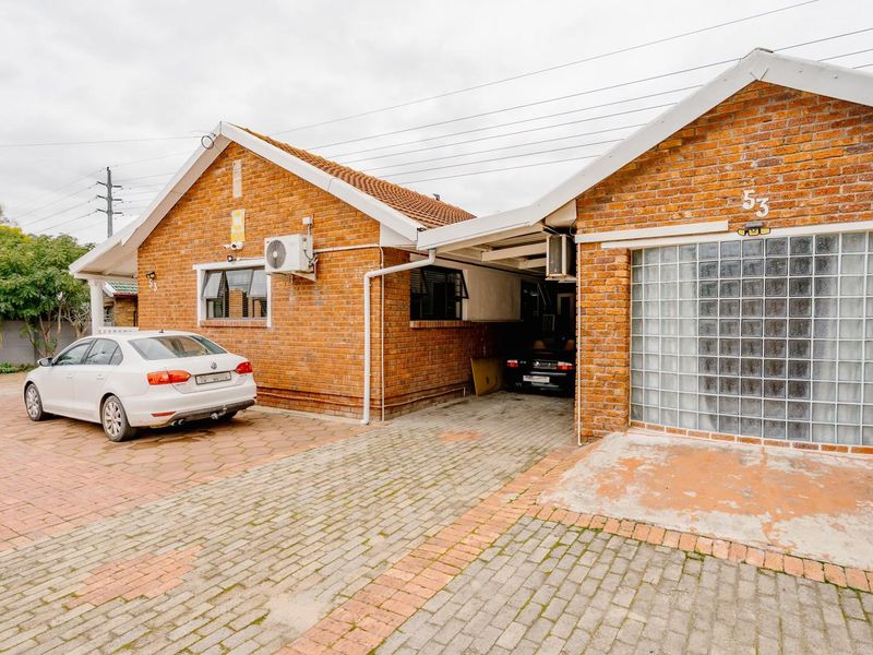 Front exterior view of a brick house featuring a paved driveway, carport, and a distinctive glass block window detail.