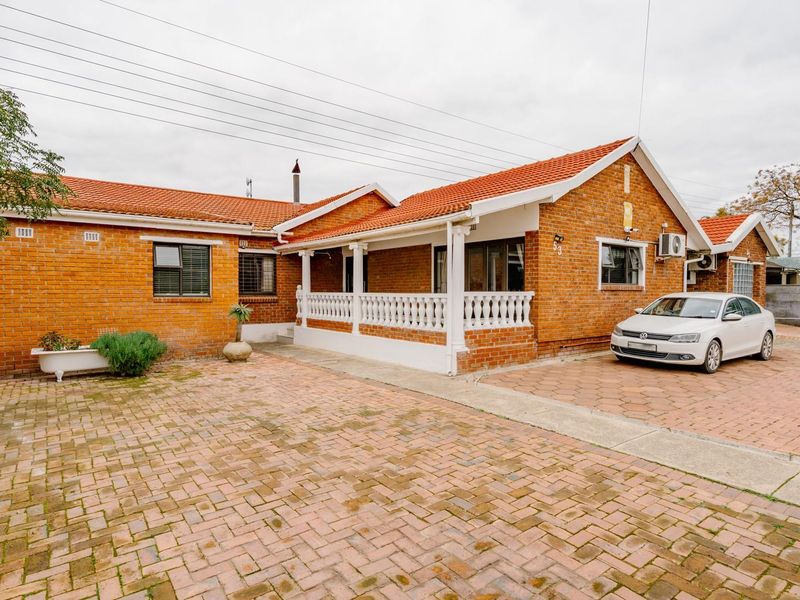 Front view of a single-story brick house featuring a tiled roof, paved driveway, and a covered patio area with a balustrade.
