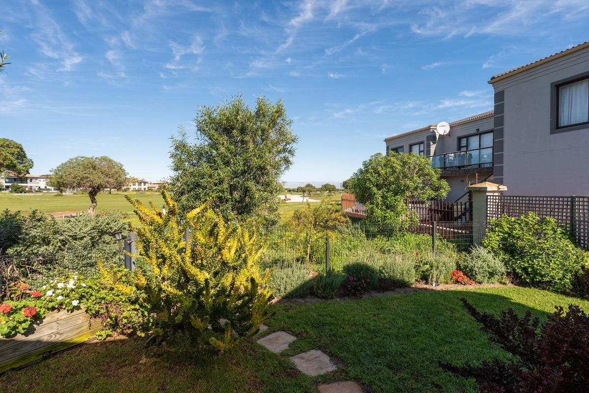 A well-maintained rear garden featuring a lawn, established landscaping, and stone pathways, with a view of the golf course and the property's rear balcony.