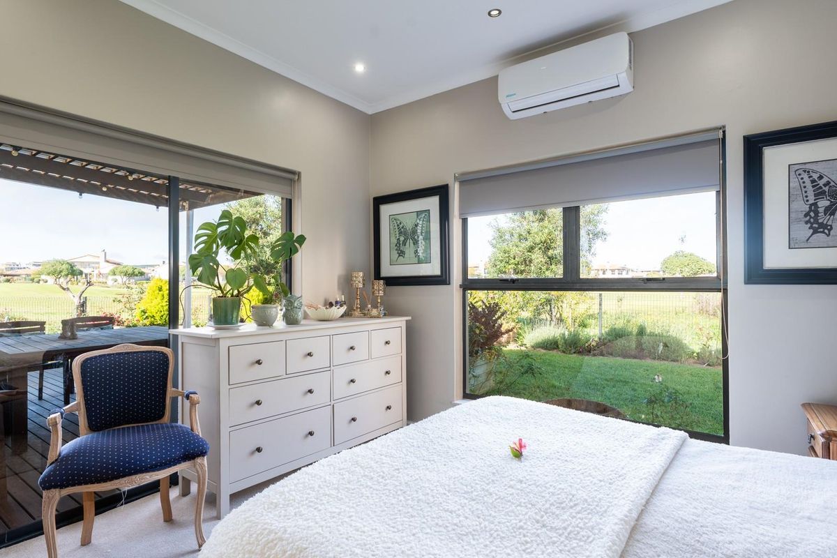 A bright bedroom featuring large windows, sliding glass doors leading to a patio, and a wall-mounted split-system air conditioner.