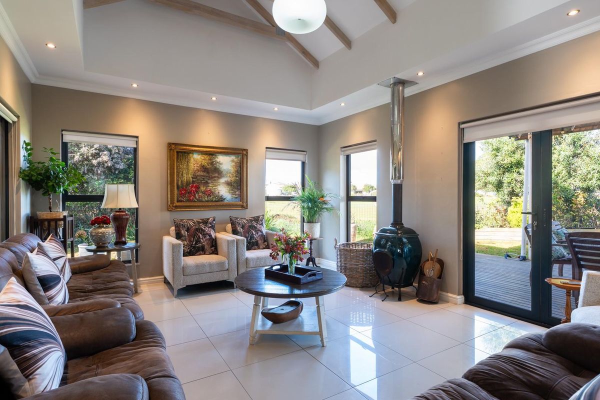 Spacious living room featuring a vaulted ceiling with exposed timber beams, tiled flooring, and a modern freestanding fireplace, with direct access to the outdoor deck.