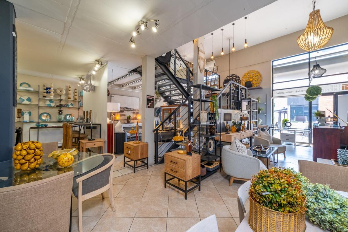 Spacious open-plan retail showroom featuring a prominent metal staircase, large display windows, and neutral tiled flooring, ideal for a high-end furniture or decor boutique.