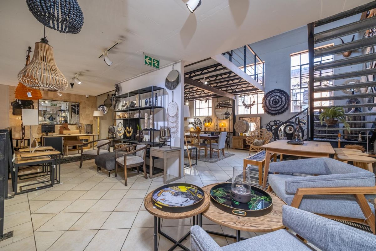 Spacious open-plan retail area featuring industrial-style architecture, a mezzanine level with a metal staircase, large windows, and tiled flooring.