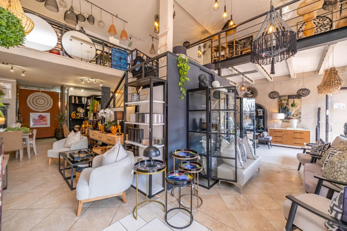 Spacious open-plan retail showroom featuring a mezzanine level, metal staircase, tiled flooring, and high ceilings with integrated lighting.