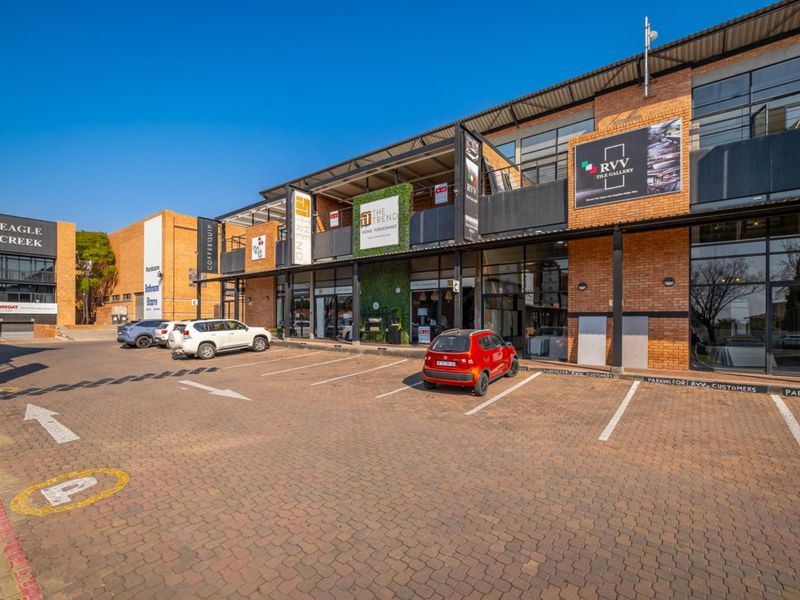 Front view of a modern multi-level retail complex featuring brick facade, large glass storefronts, and dedicated paved parking bays.