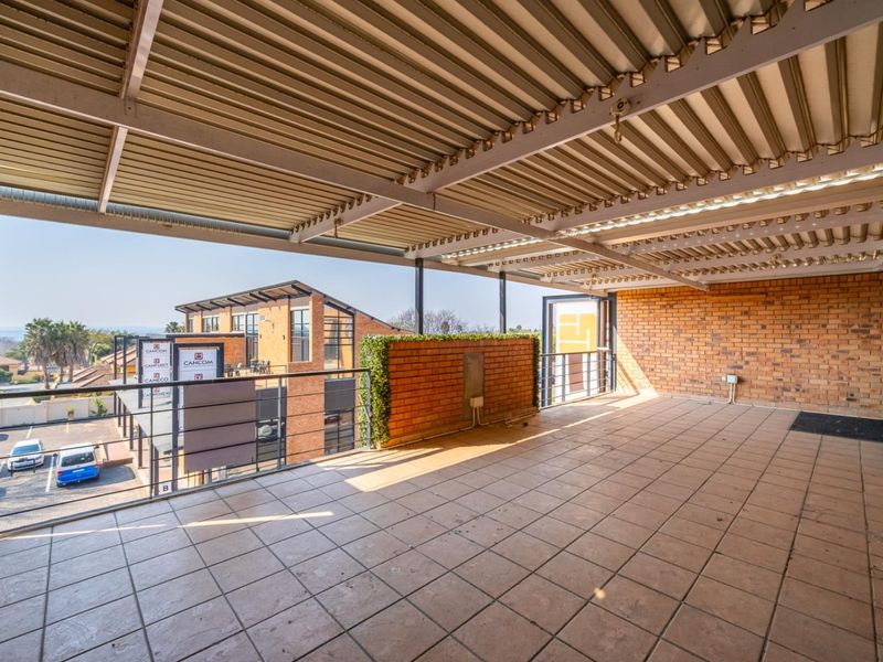 Spacious covered balcony featuring tiled flooring, brick wall accents, and metal railing, offering an open-air space suitable for outdoor seating or commercial use.