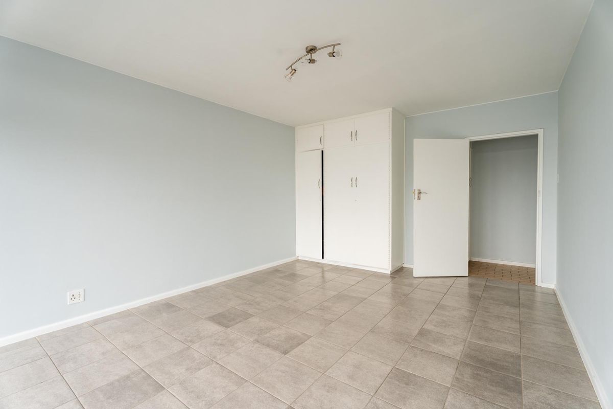 A clean, empty bedroom featuring neutral tiled flooring, built-in cupboards, and light blue walls, offering a versatile space ready for personalization.