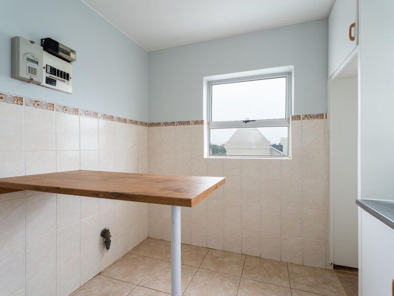 A functional laundry area featuring tiled walls, a fixed wooden work surface, plumbing connections, and built-in cabinetry.