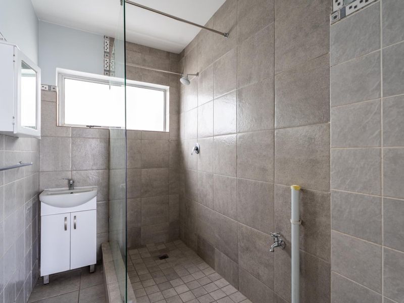 A functional bathroom featuring a walk-in shower with glass screen, wall-mounted vanity, and neutral floor-to-ceiling tiling.