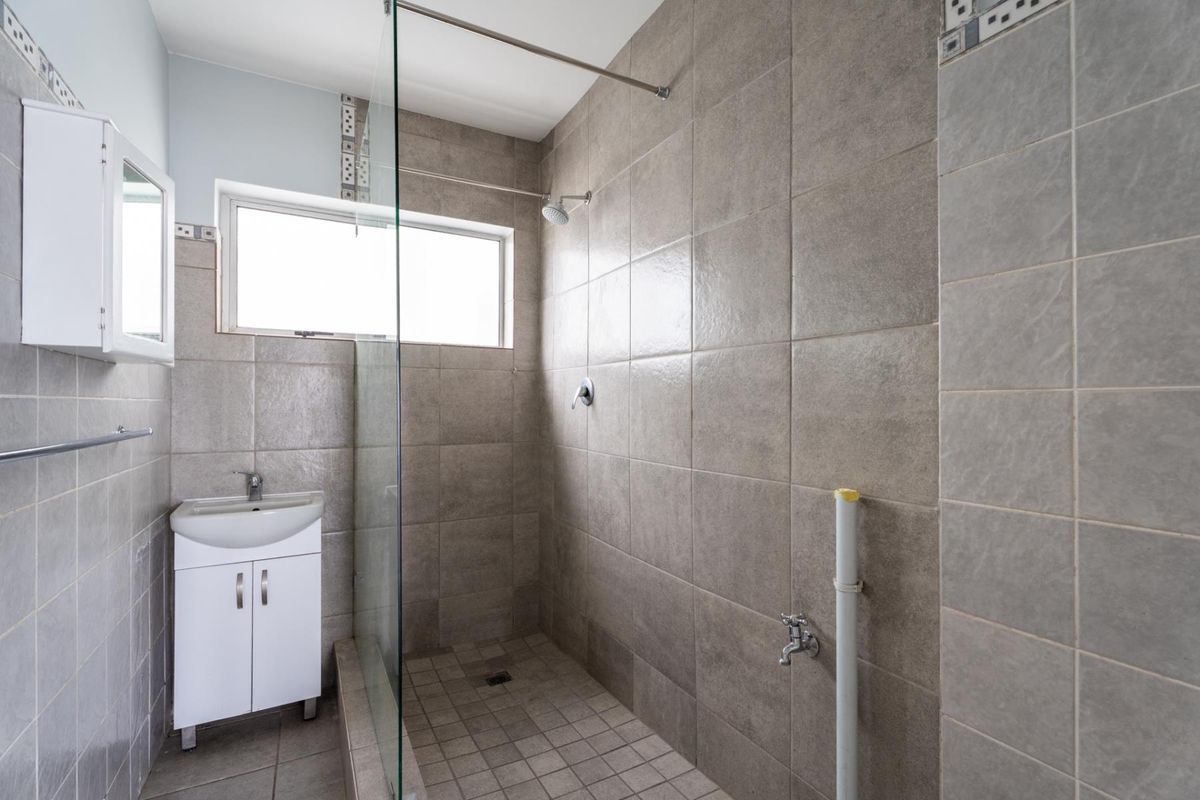 A functional bathroom featuring a walk-in shower with glass screen, wall-mounted vanity, and neutral floor-to-ceiling tiling.