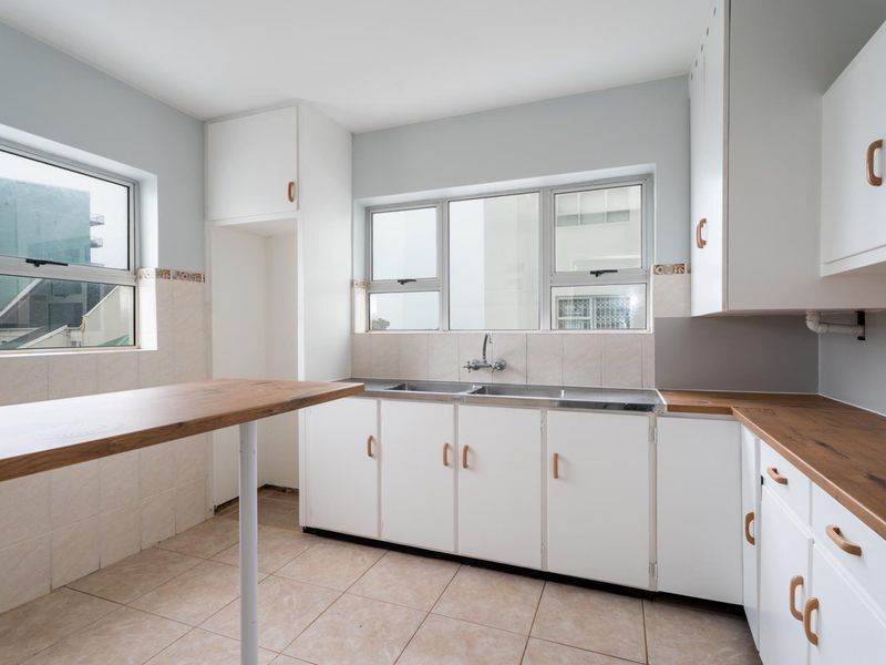A bright, empty kitchen featuring white cabinetry, wood-look laminate countertops, a double basin sink, and tiled flooring with a breakfast bar.