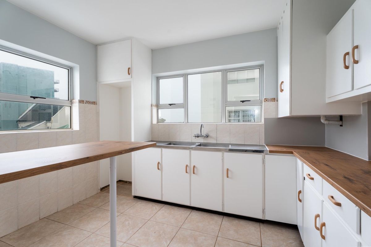 A bright, empty kitchen featuring white cabinetry, wood-look laminate countertops, a double basin sink, and tiled flooring with a breakfast bar.