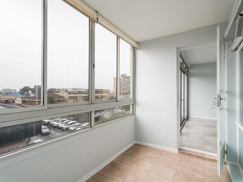 An enclosed balcony featuring tiled flooring and large aluminium sliding windows, offering an airy space with views of the surrounding area.
