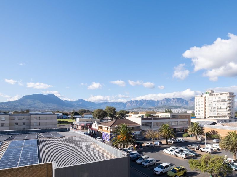 An elevated panoramic view overlooking the surrounding urban landscape, parking areas, and distant mountain ranges under a clear blue sky.