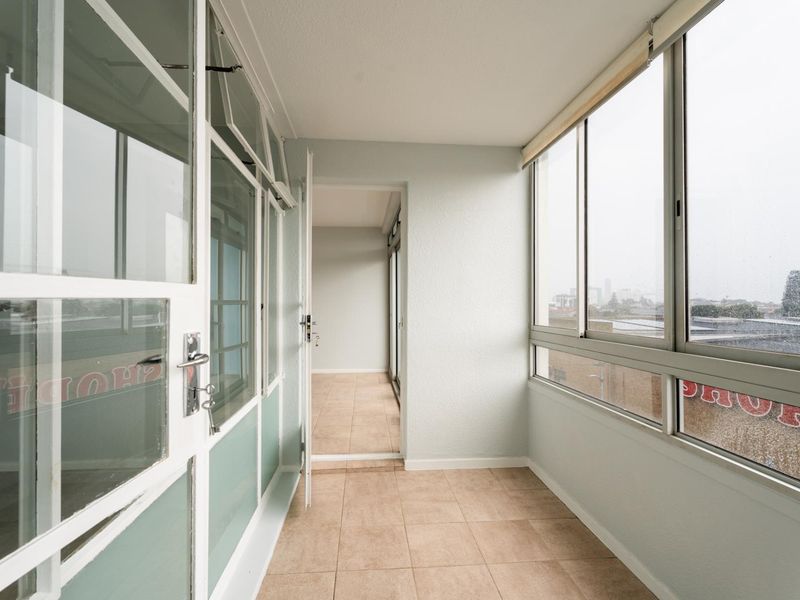 An enclosed balcony featuring tiled flooring and large windows, offering a bright, versatile space with views of the surrounding area.
