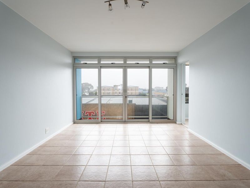 An empty, light-filled living room featuring neutral tiled flooring and large sliding glass doors that open to an outdoor balcony area.