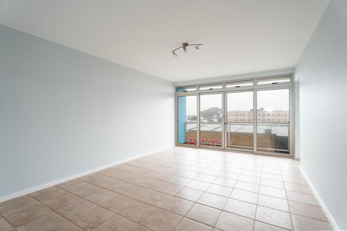 A bright, empty living room featuring neutral tiled flooring and large sliding glass doors that provide access to an outdoor balcony area.