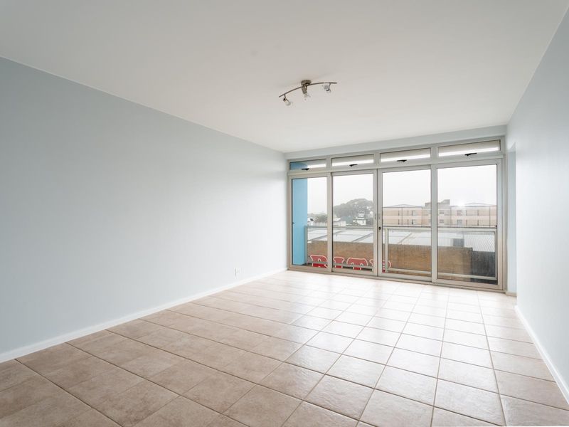 A bright, empty living room featuring neutral tiled flooring and large sliding glass doors that provide access to an outdoor balcony area.