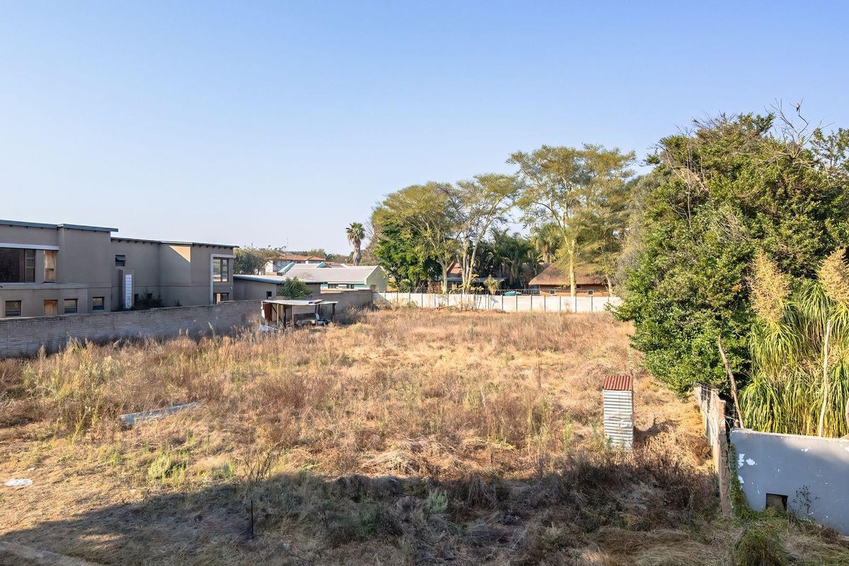 A vacant residential plot featuring dry vegetation, enclosed by perimeter walls and boundary fencing, offering a clear space for future development.