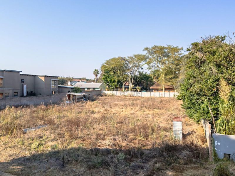 A vacant residential plot featuring dry vegetation, enclosed by perimeter walls and boundary fencing, offering a clear space for future development.