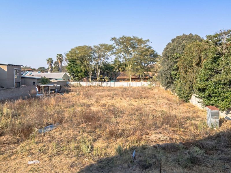A vacant residential plot featuring perimeter walling, established trees, and open land, offering a blank canvas for future development.