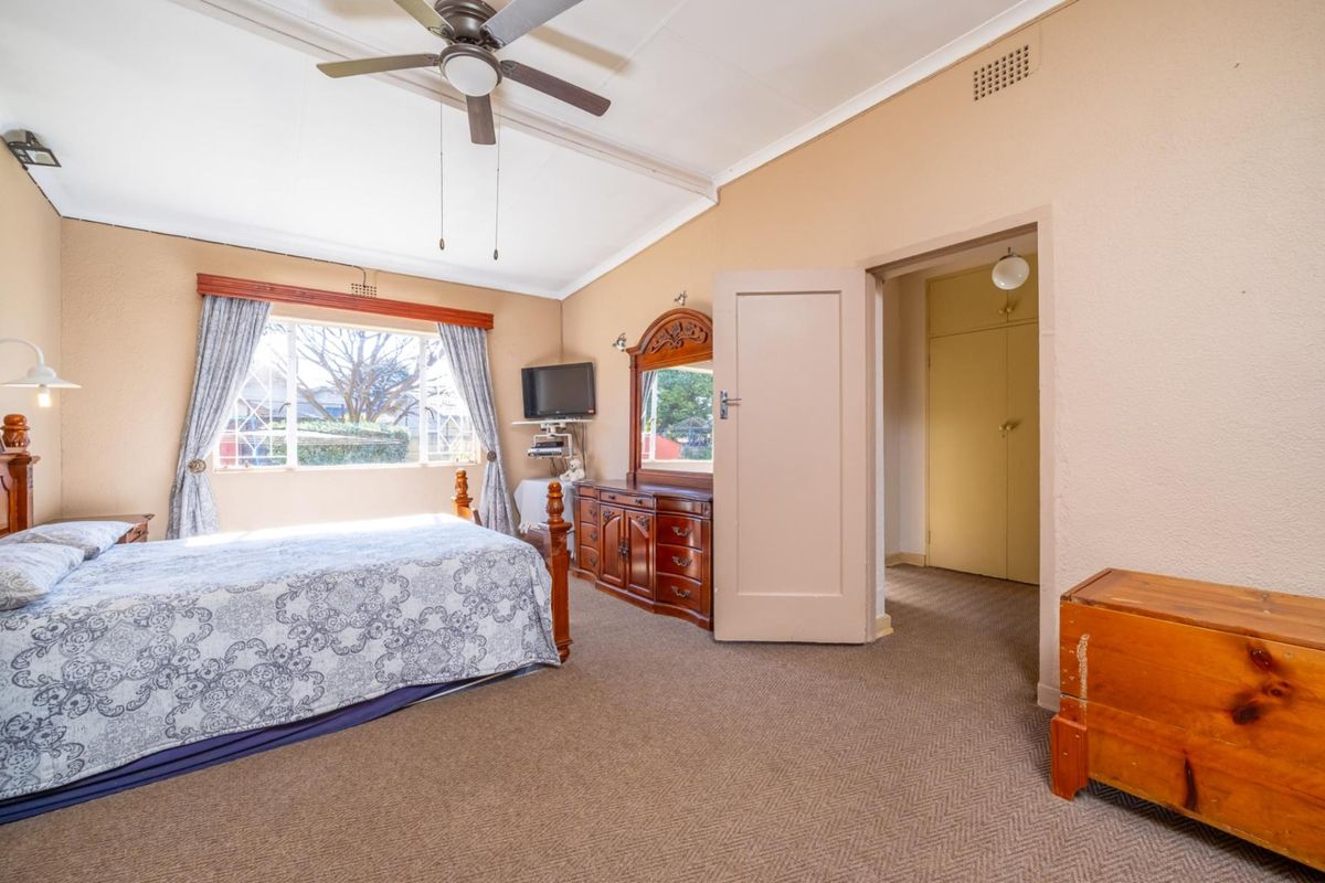 A spacious bedroom featuring carpeted flooring, a ceiling fan, and a built-in cupboard, offering a functional and comfortable living space.