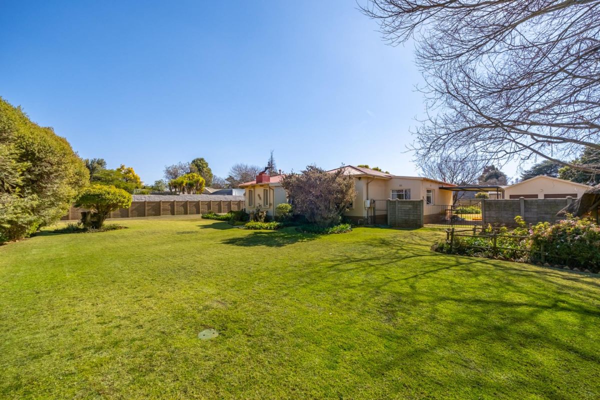 Spacious rear garden featuring a well-maintained lawn, established landscaping, and a clear view of the property's rear elevation and detached garage.