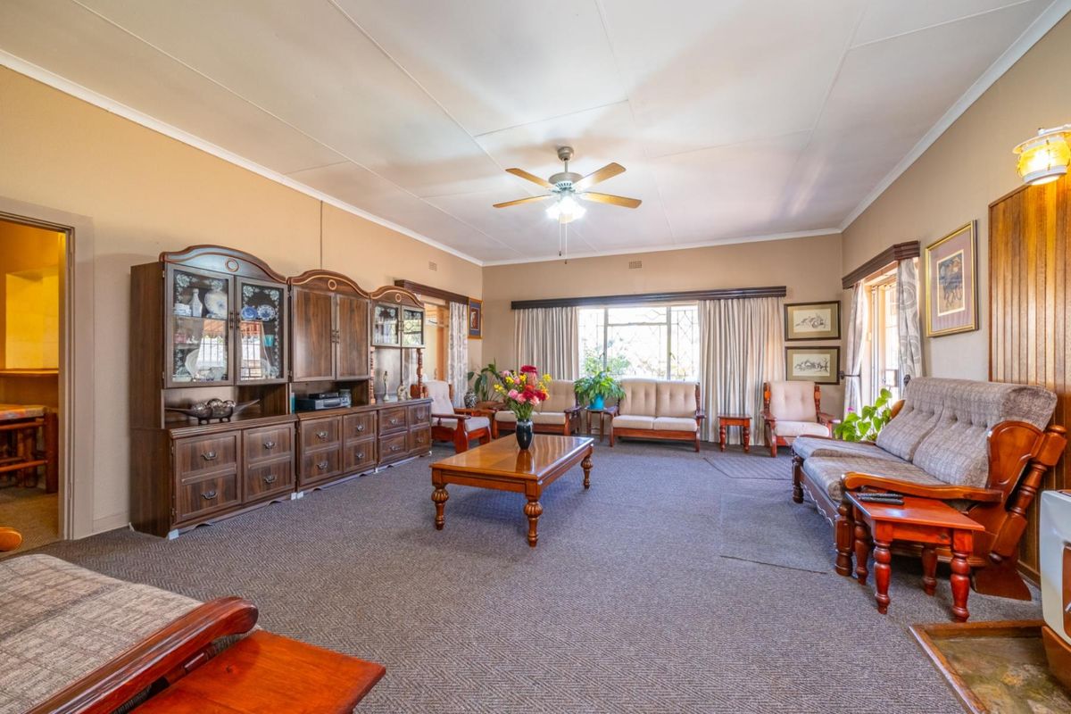 Spacious living room featuring carpeted flooring, a ceiling fan, and timber wall paneling, offering a traditional layout with ample natural light.