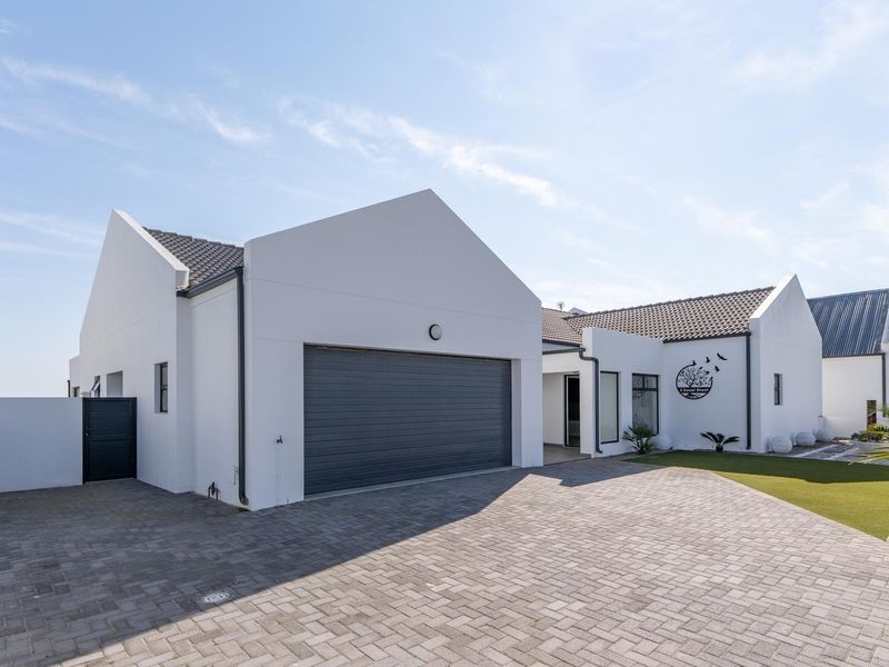 Modern single-story residence featuring a clean white facade, gabled roofline, paved driveway, and an integrated garage.