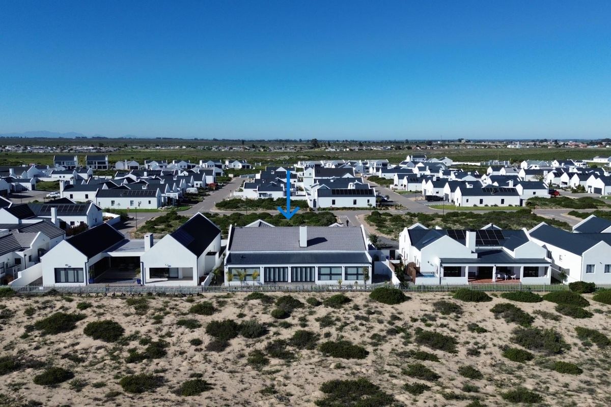Aerial view of a modern residential property in a coastal estate, featuring a tiled roof with solar panels and proximity to natural dunes.