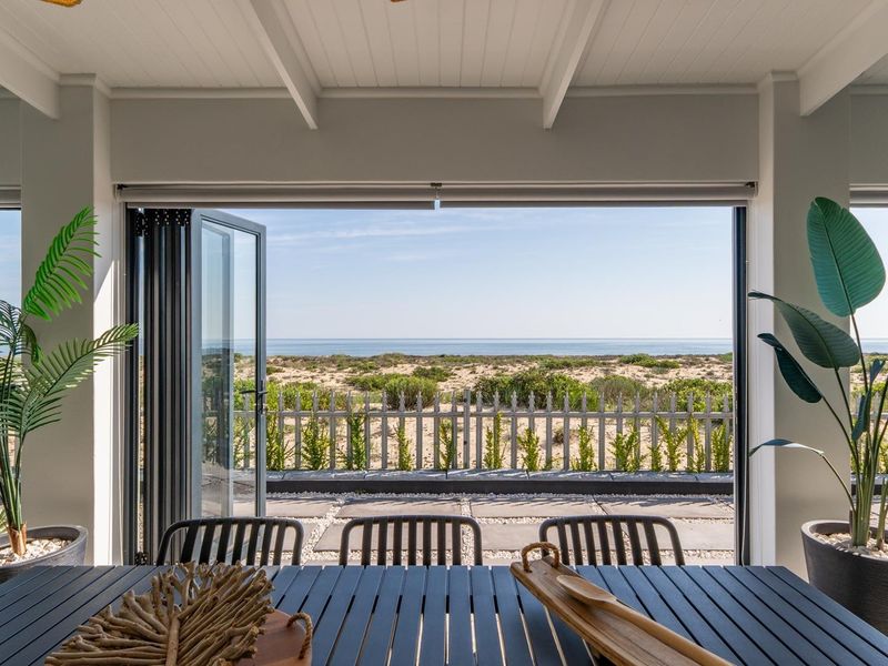 A covered patio featuring bi-fold doors that open to a scenic coastal view, complete with a paved outdoor area and picket fencing.