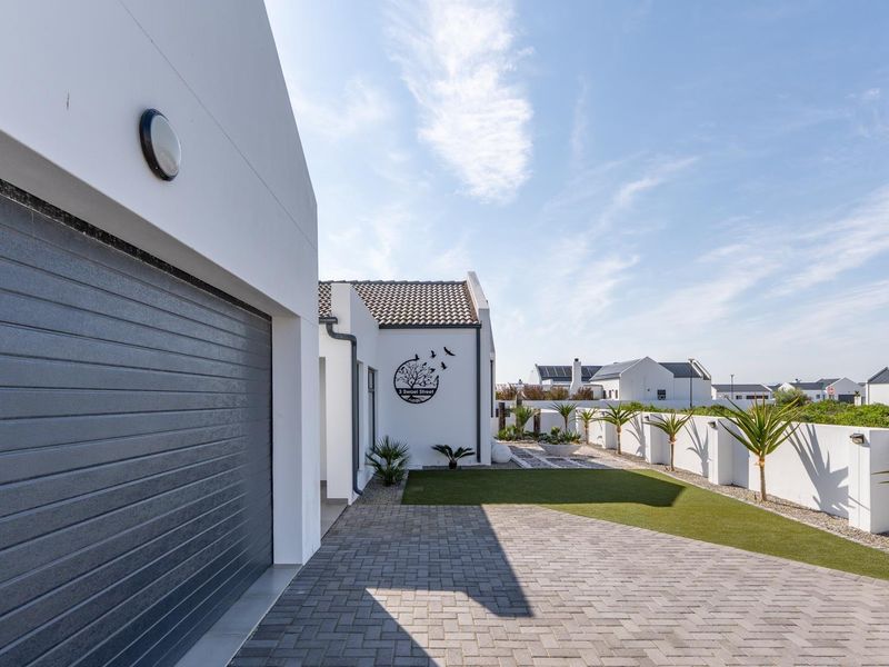 Modern front elevation featuring a paved driveway, automated garage door, and clean white boundary walls with landscaped garden elements.