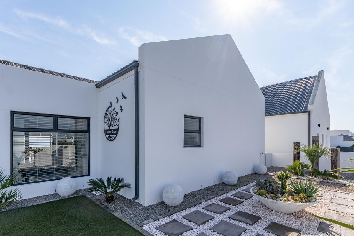 A well-maintained rear exterior view of a modern home featuring clean white walls, dark aluminium window frames, and landscaped gravel garden areas.