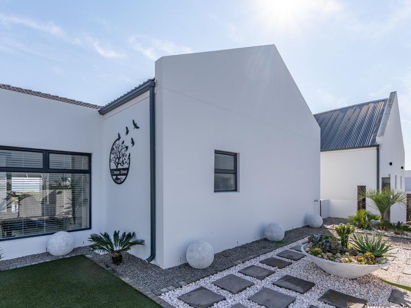 A well-maintained rear exterior view of a modern home featuring clean white walls, dark aluminium window frames, and landscaped gravel garden areas.