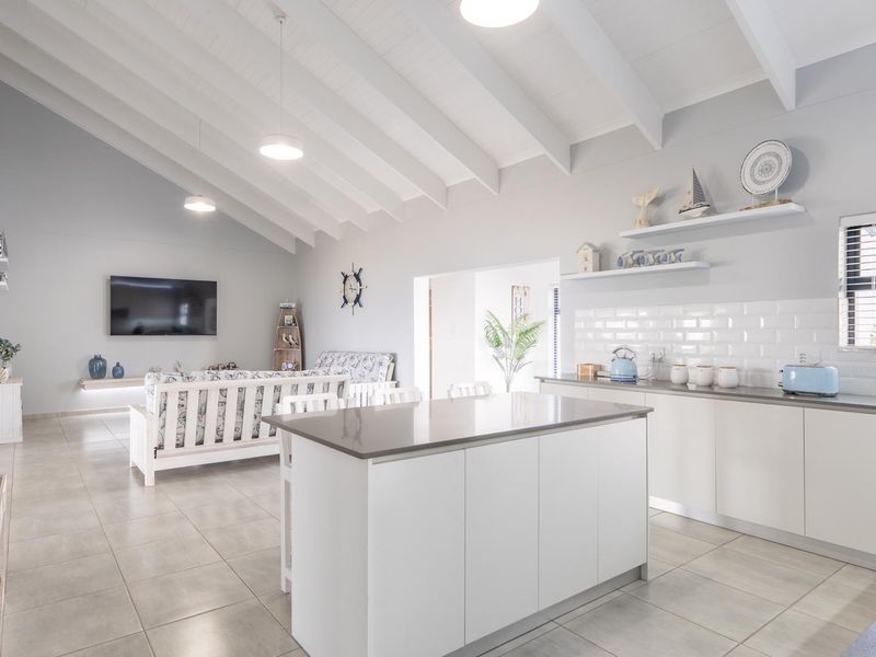 Spacious open-plan living and kitchen area featuring a modern kitchen island, subway tile backsplash, and high vaulted ceilings with exposed beams.