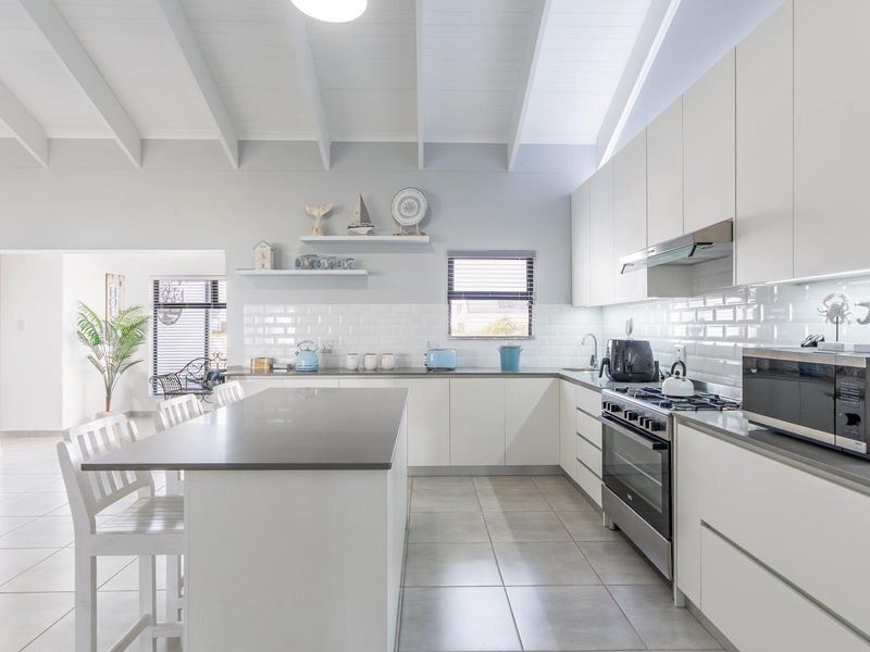 Modern, bright kitchen featuring a large central island, subway tile backsplash, stainless steel appliances, and a high vaulted ceiling with exposed beams.