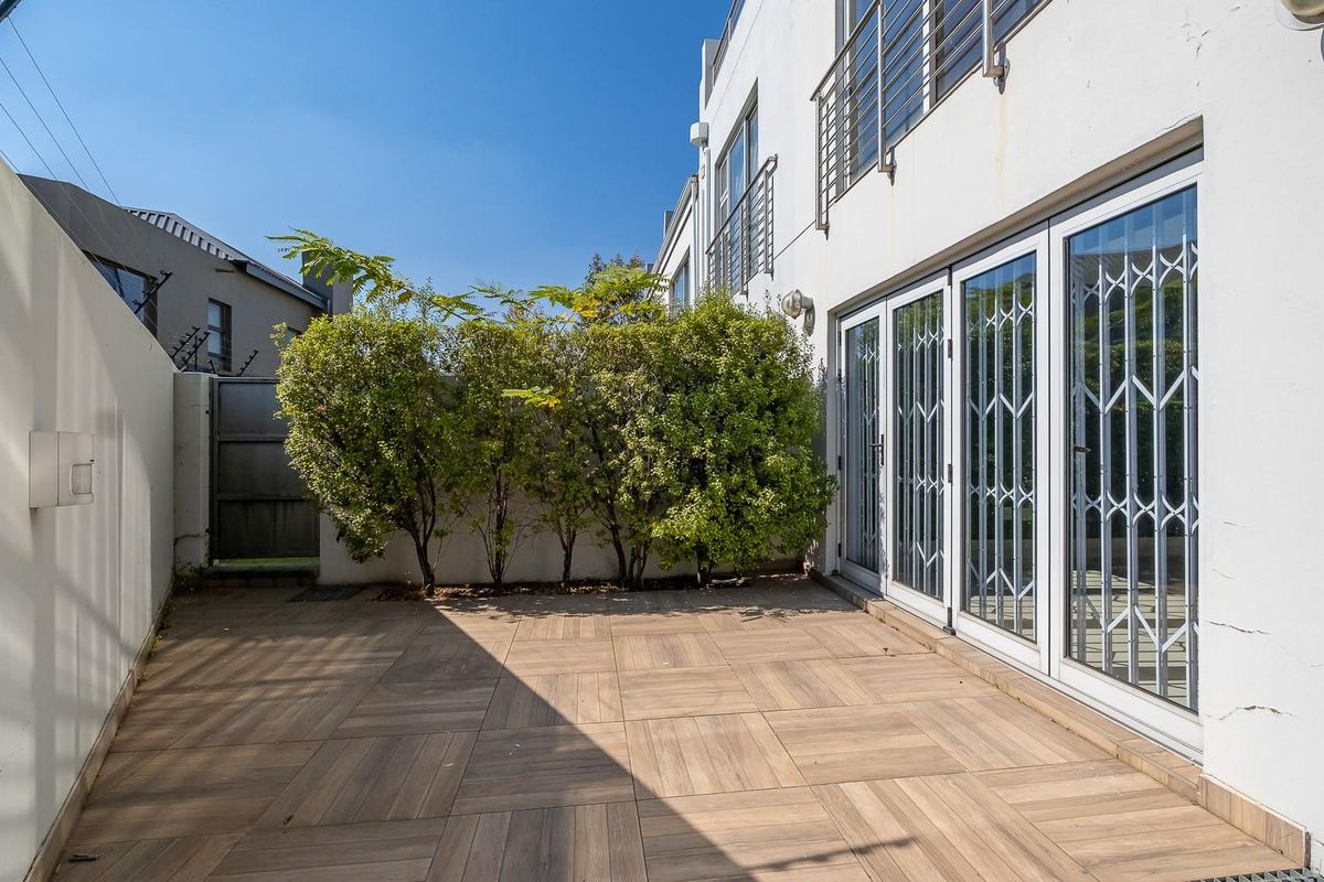 A private rear patio area featuring tiled flooring, secure sliding glass doors, and a boundary wall with electric fencing.
