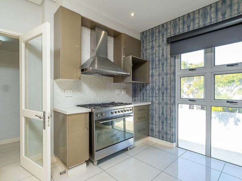 Modern kitchen featuring high-gloss cabinetry, a stainless steel gas stove with extractor fan, mosaic backsplash, and large windows providing ample natural light.