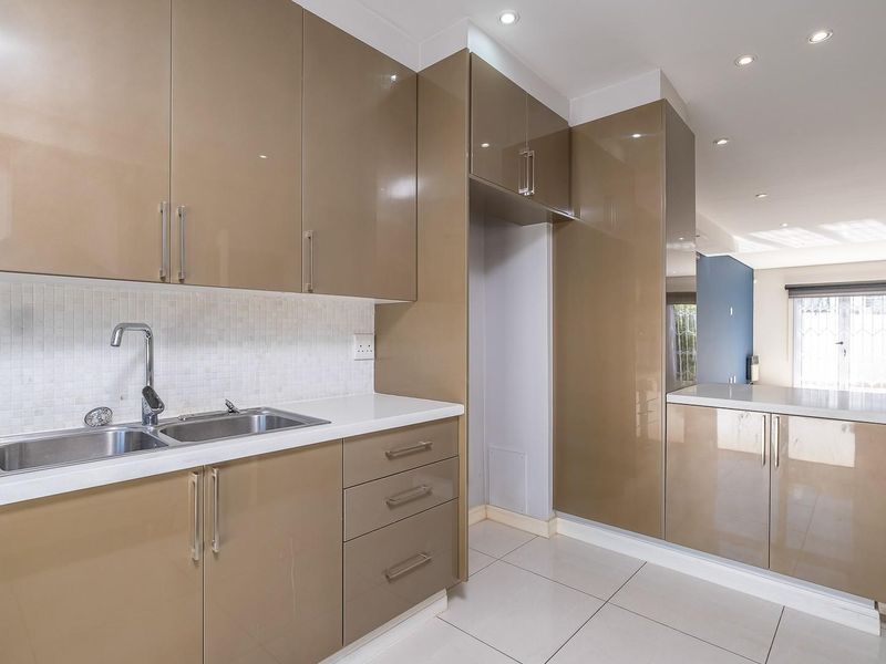 Modern kitchen featuring high-gloss cabinetry, stone countertops, a double bowl sink, and a mosaic tile backsplash, finished with clean tiled flooring.