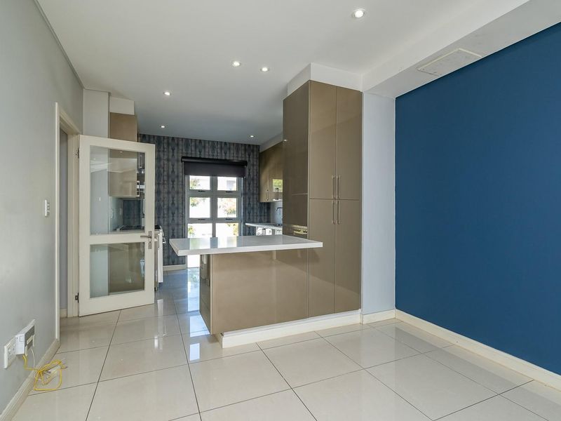 Modern open-plan living area featuring sleek glossy cabinetry, a breakfast bar, and neutral tiled flooring with a bold blue accent wall.