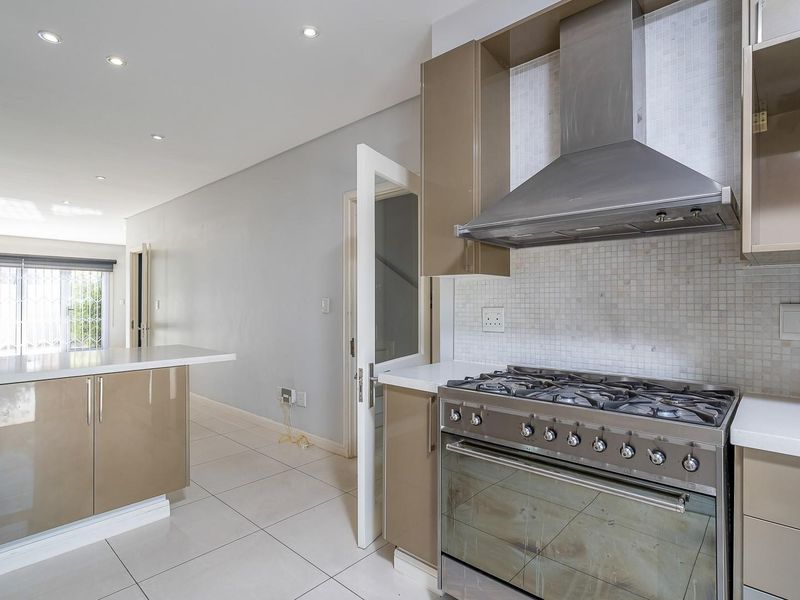 Modern kitchen featuring high-gloss cabinetry, stone countertops, a gas stove with stainless steel extractor fan, and neutral mosaic tile backsplash.