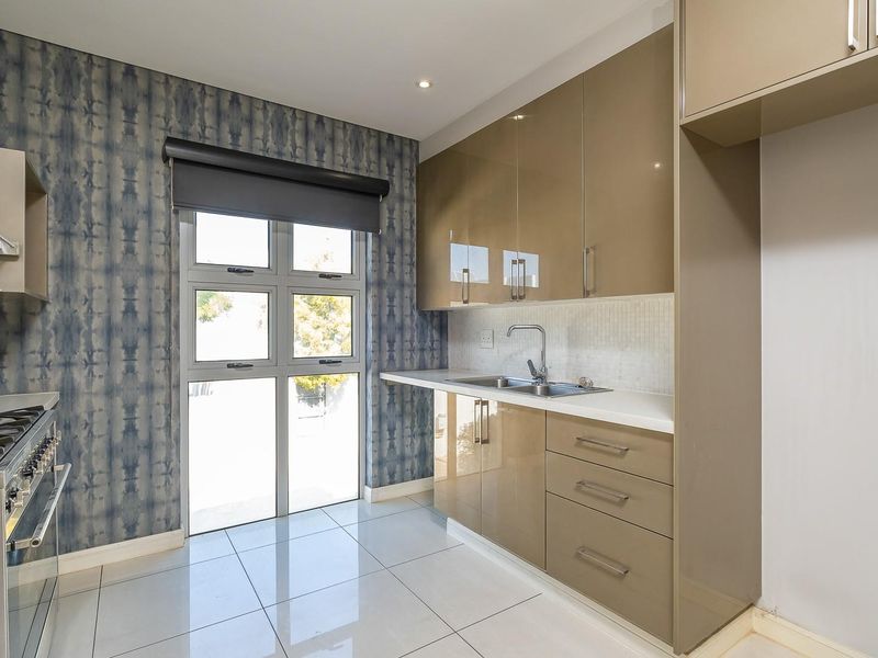 Modern kitchen featuring high-gloss cabinetry, gas hob, extractor fan, stainless steel sink, and tiled flooring with direct access to the exterior.