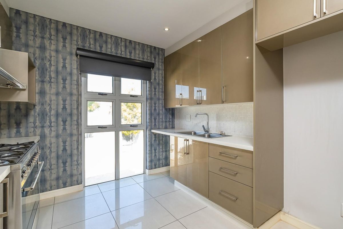 Modern kitchen featuring high-gloss cabinetry, gas hob, extractor fan, stainless steel sink, and tiled flooring with direct access to the exterior.