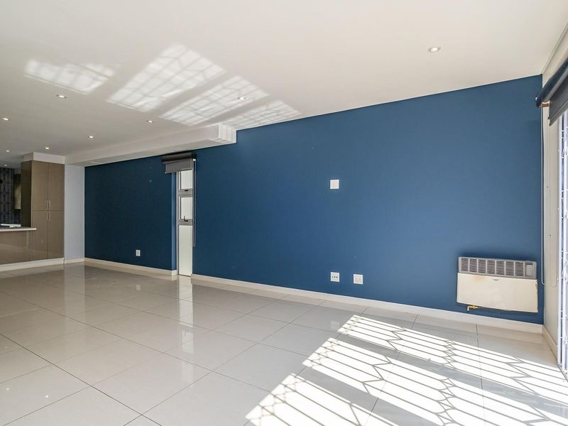Spacious open-plan living area featuring polished porcelain tiles, a feature blue wall, wall-mounted heater, and a modern kitchen with integrated cabinetry.