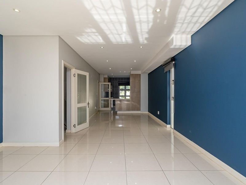 Spacious open-plan living area featuring polished porcelain floor tiles, recessed lighting, and a neutral color palette with a bold blue accent wall.