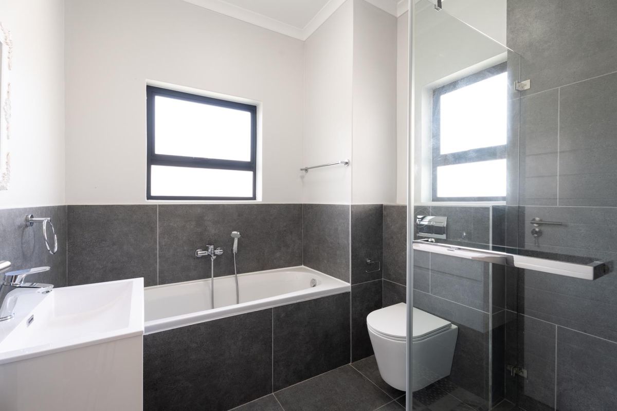 Modern bathroom featuring a built-in bathtub, wall-hung toilet, glass shower enclosure, and contemporary grey tiling throughout.