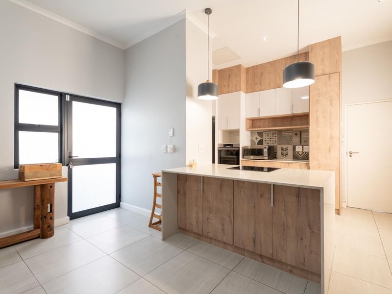 Modern kitchen featuring a central island with integrated cooktop, sleek wood-tone and white cabinetry, tiled flooring, and contemporary pendant lighting.