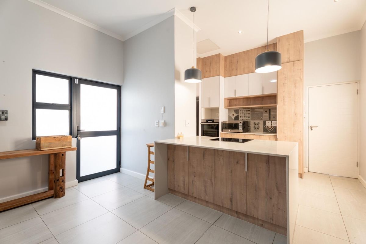 Modern kitchen featuring a central island with integrated cooktop, sleek wood-tone and white cabinetry, tiled flooring, and contemporary pendant lighting.