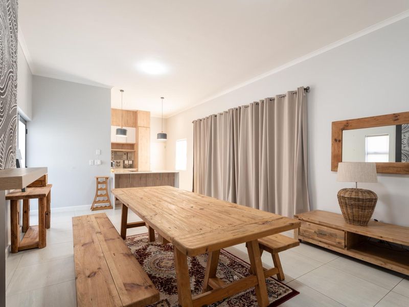 An open-plan living and dining area featuring light-toned tiled flooring, neutral walls, and a modern kitchen with wood-finish cabinetry.